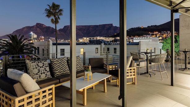 A rooftop terrace with outdoor seating, a palm tree, and a view of a cityscape and mountains. - Protea Hotel by Marriott Cape Town Waterfront Breakwater Lodge (Cape Town)
