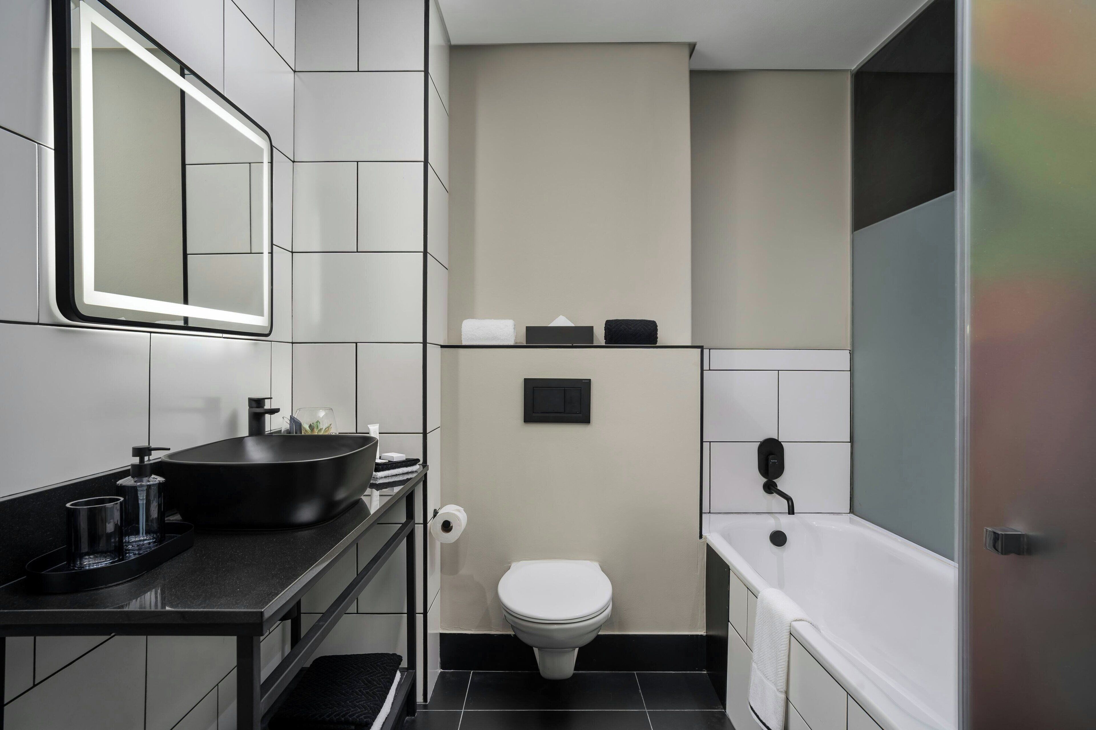 A modern bathroom with a black sink, a toilet, and a bathtub.