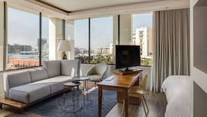 A modern hotel room with a large window, a sofa, a desk, a TV, and a bed. - Protea Hotel by Marriott Cape Town Waterfront Breakwater Lodge (Cape Town)