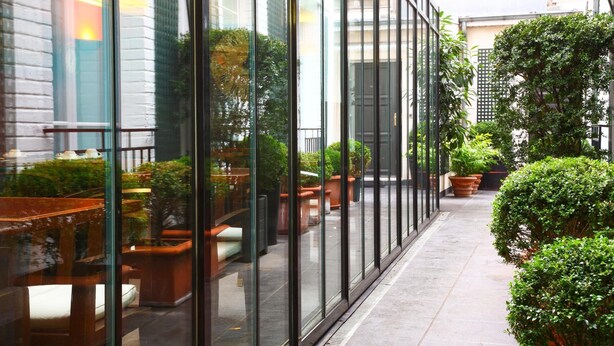 A corridor with glass walls, potted plants, and outdoor seating. - Hotel De La Jatte (Neuilly-sur-Seine)