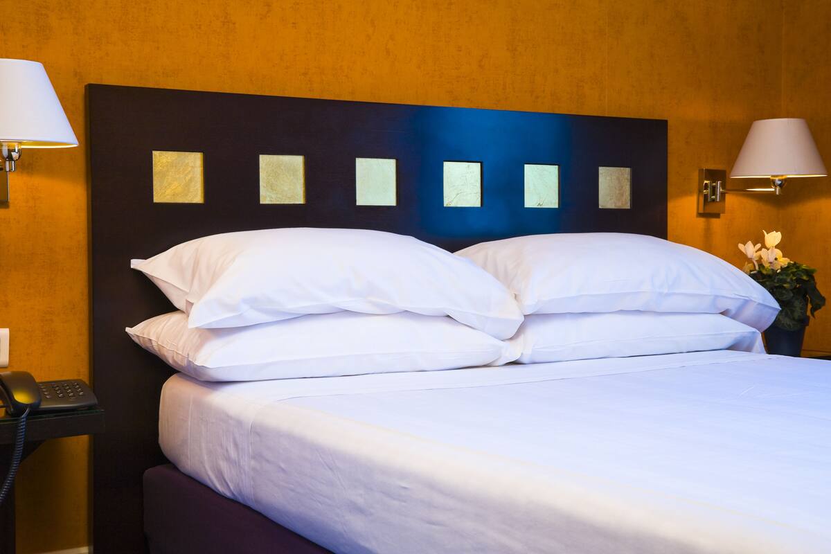 A hotel room with a large bed, white linens, a dark headboard, and two wall-mounted lamps.