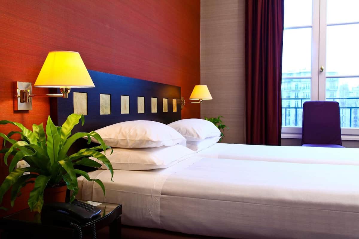 A hotel room with a bed, two bedside lamps, a potted plant, and a telephone on a side table.