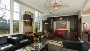 A spacious living room with leather sofas, a coffee table, and a fireplace. There are large windows providing a view of the outdoors. - Hotel De La Jatte (Neuilly-sur-Seine)