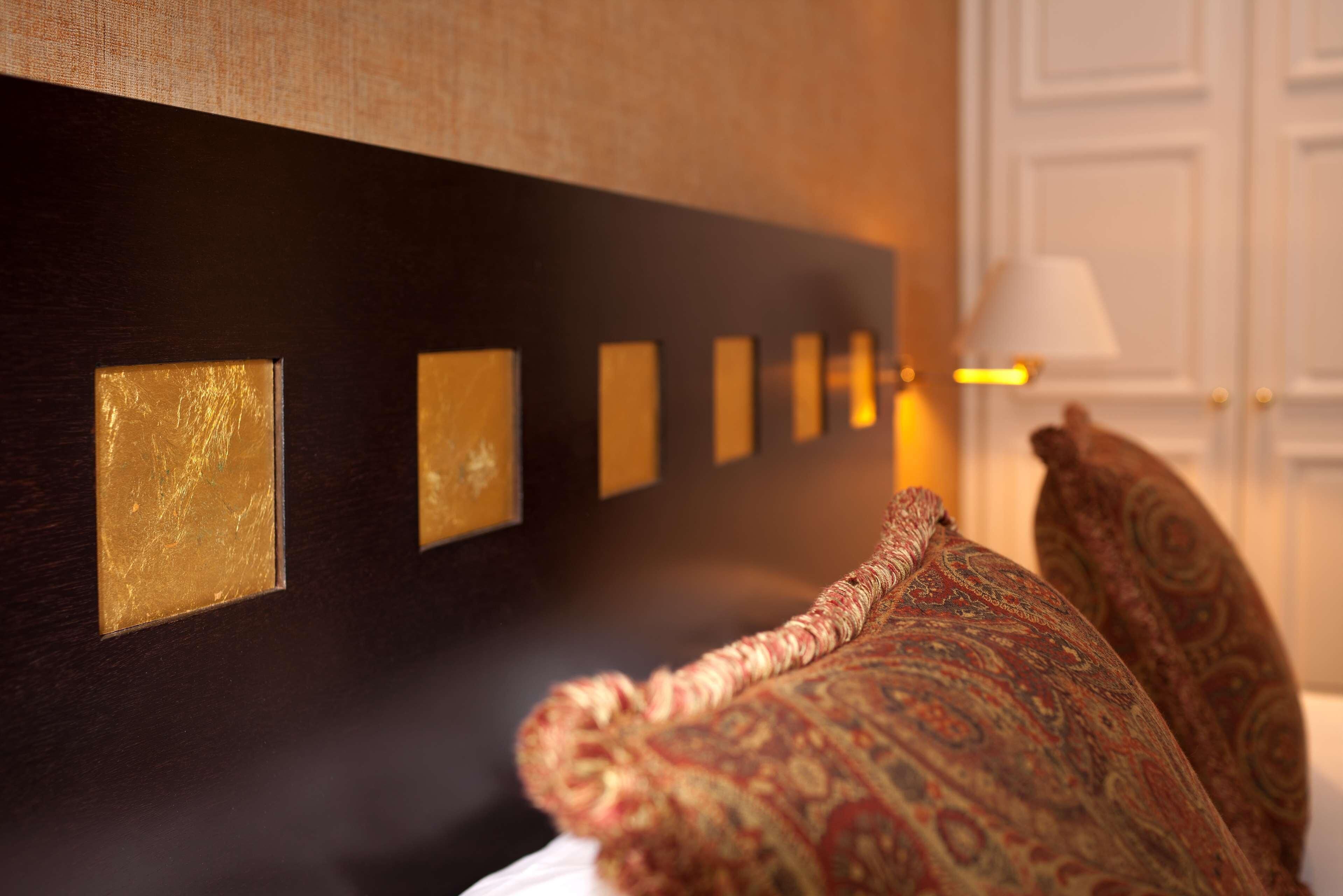 A room with a dark wooden headboard, a series of rectangular gold-colored panels, and a patterned throw pillow.