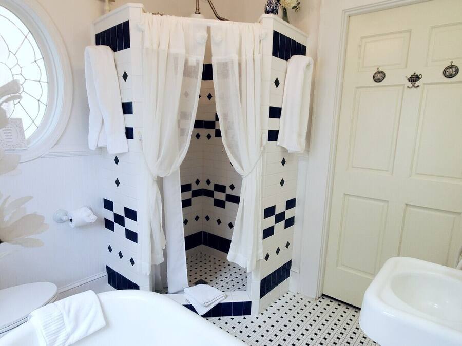 Un baño con un lavamanos blanco, un inodoro blanco, una bañera blanca, una ducha blanca con diseño de cuadros y una puerta blanca con ventana.