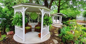 Relax in a serene garden setting surrounded by lush greenery and a charming gazebo.