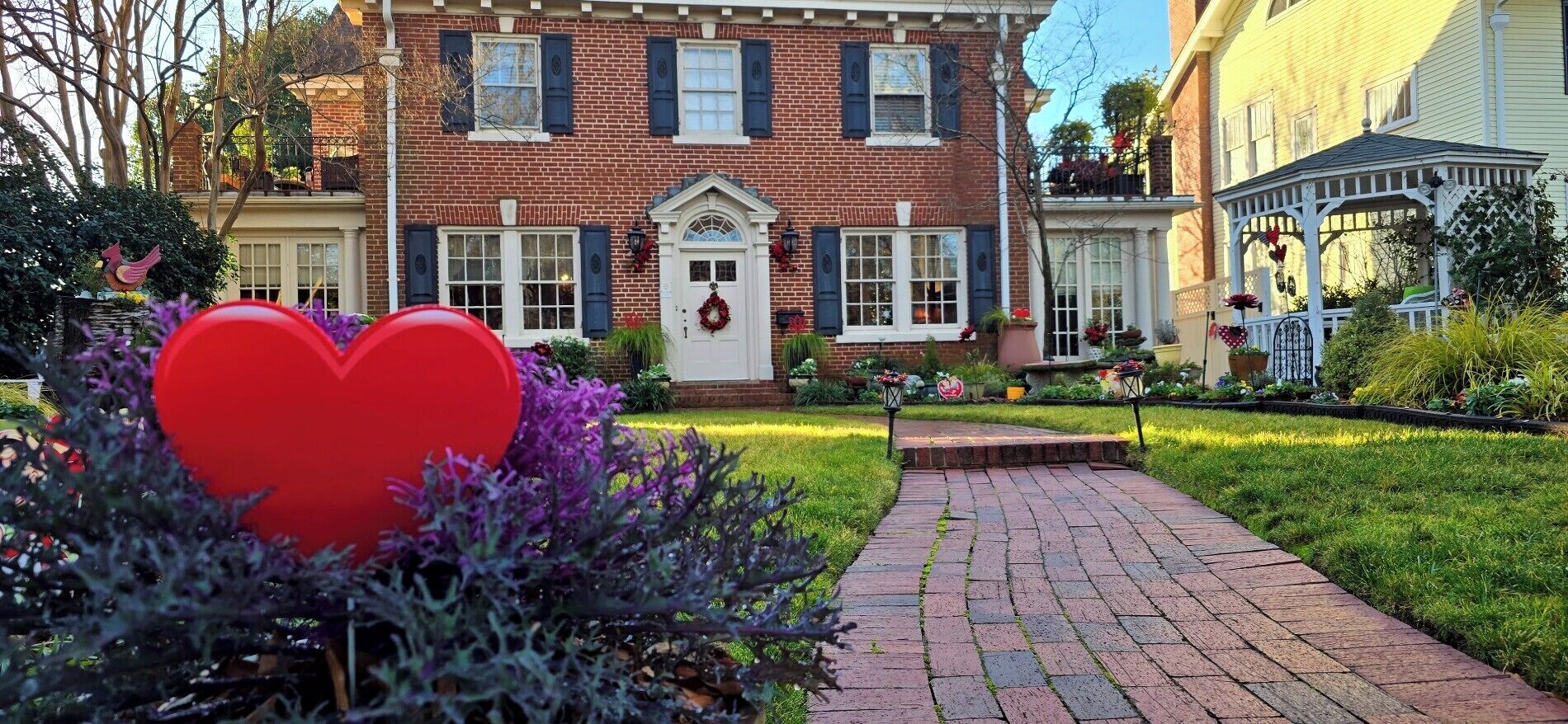 A brick building with a front porch, a garden with a pathway, and a gazebo.