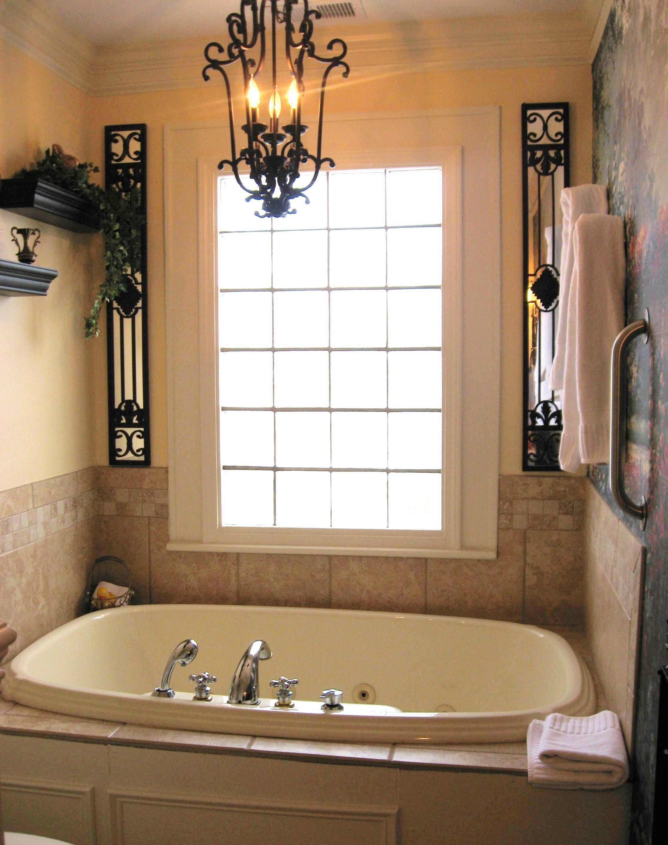 A bathroom with a large bathtub, a window with a grid pattern, a chandelier, and a towel rack.