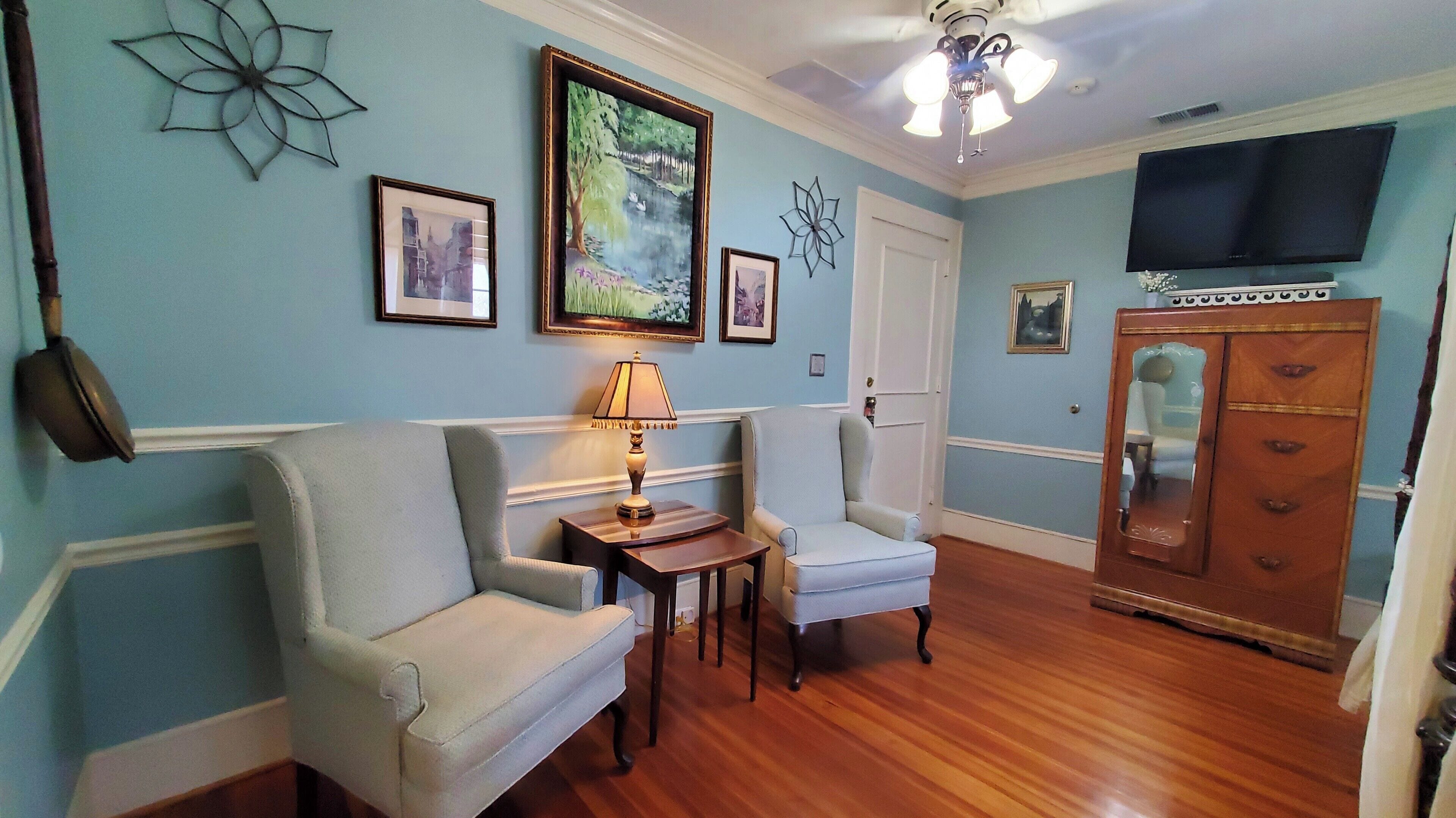 A living room with two armchairs, a wooden cabinet, a television, and wall art.