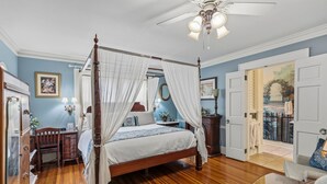A four-poster bed with white drapes, a wooden desk, a chair, and a small table. - Pettigru Place Bed & Breakfast (Greenville)