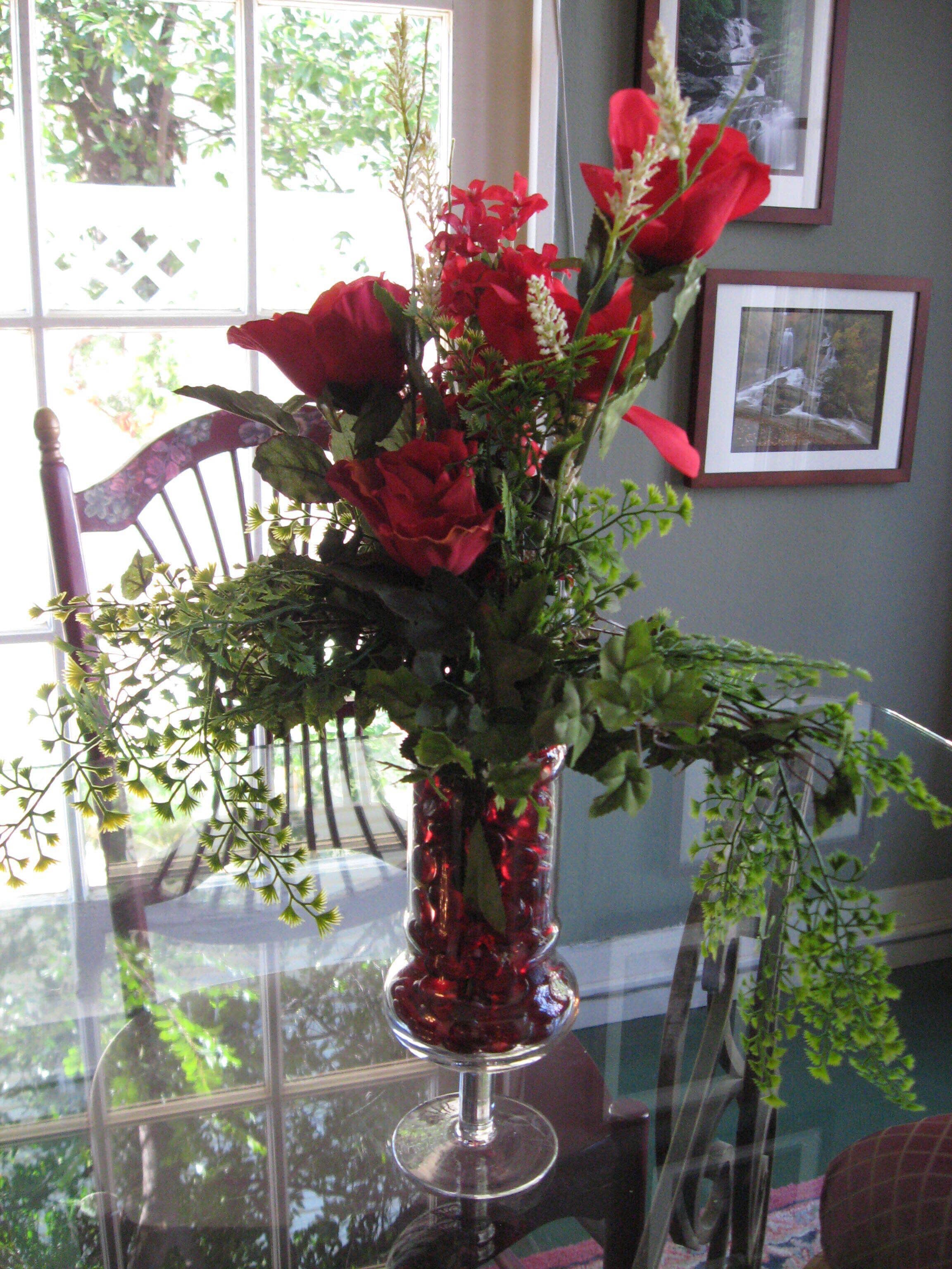 Un vase rouge orné de fleurs, posé sur une table en verre.