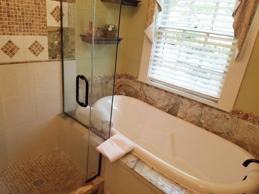 Une salle de bain avec une douche à parois de verre, une baignoire et une fenêtre équipée de stores.