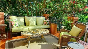 Relax in a serene patio surrounded by lush greenery, featuring a comfortable sofa and wicker chair.