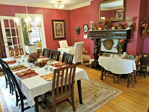 Classic dining room with a long table set for a meal, featuring a chandelier, fireplace, and mirror.