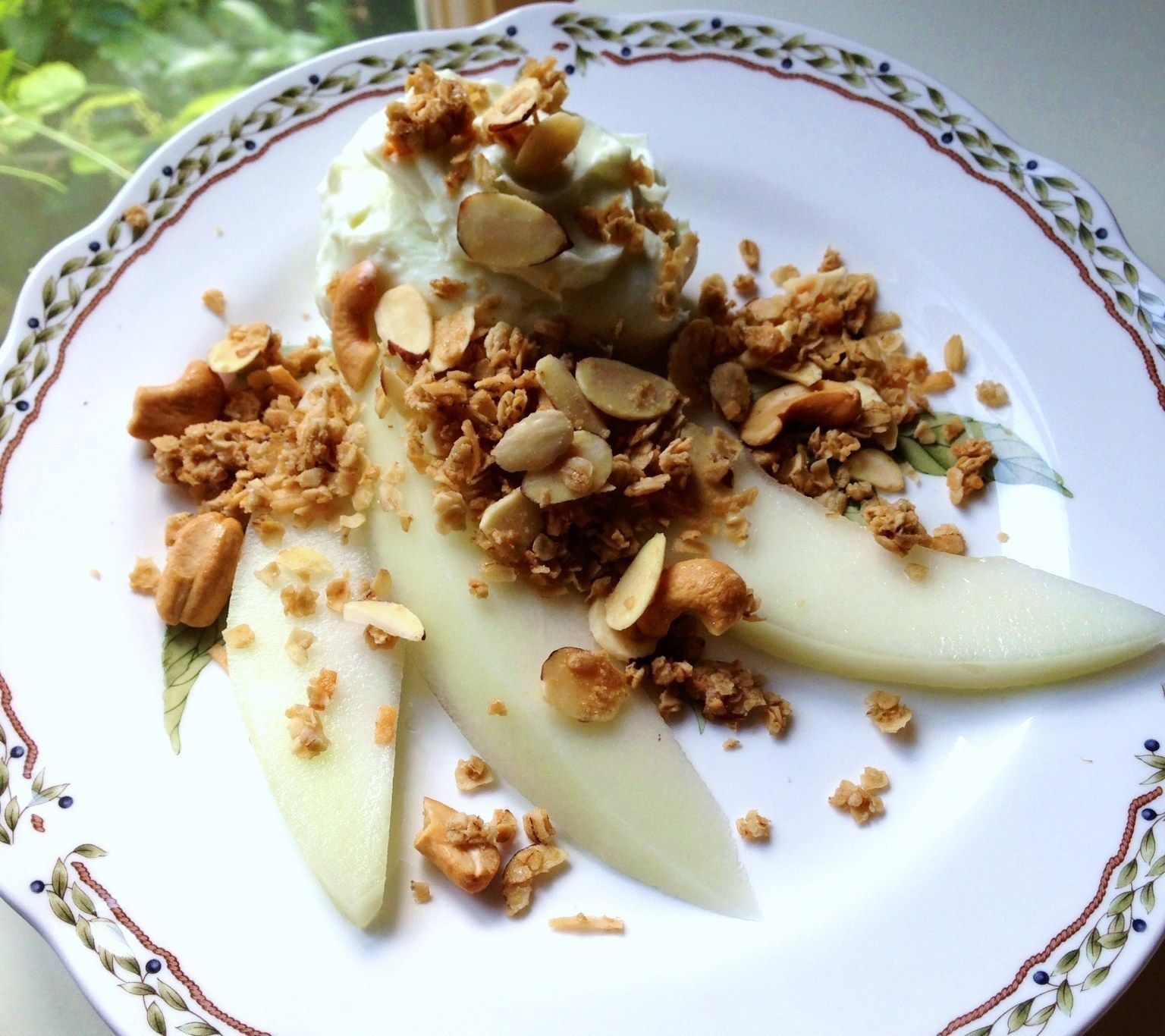 A plate with sliced pears, granola, and almonds.