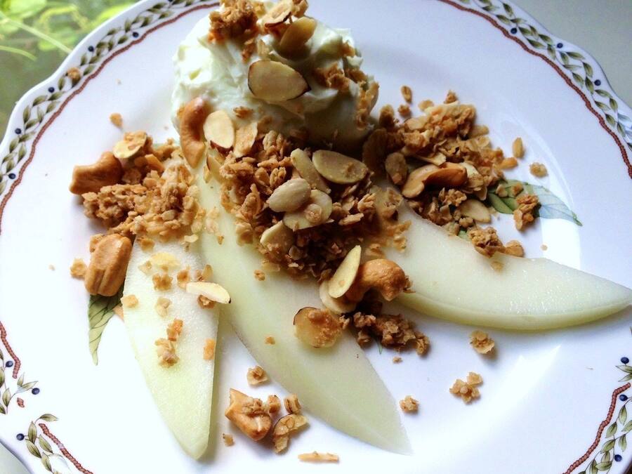 A plate with sliced pears, granola, and almonds.
