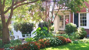 A garden with a white picket fence, red and white flowers, and a brick house with a porch. - Pettigru Place Bed & Breakfast (Greenville)
