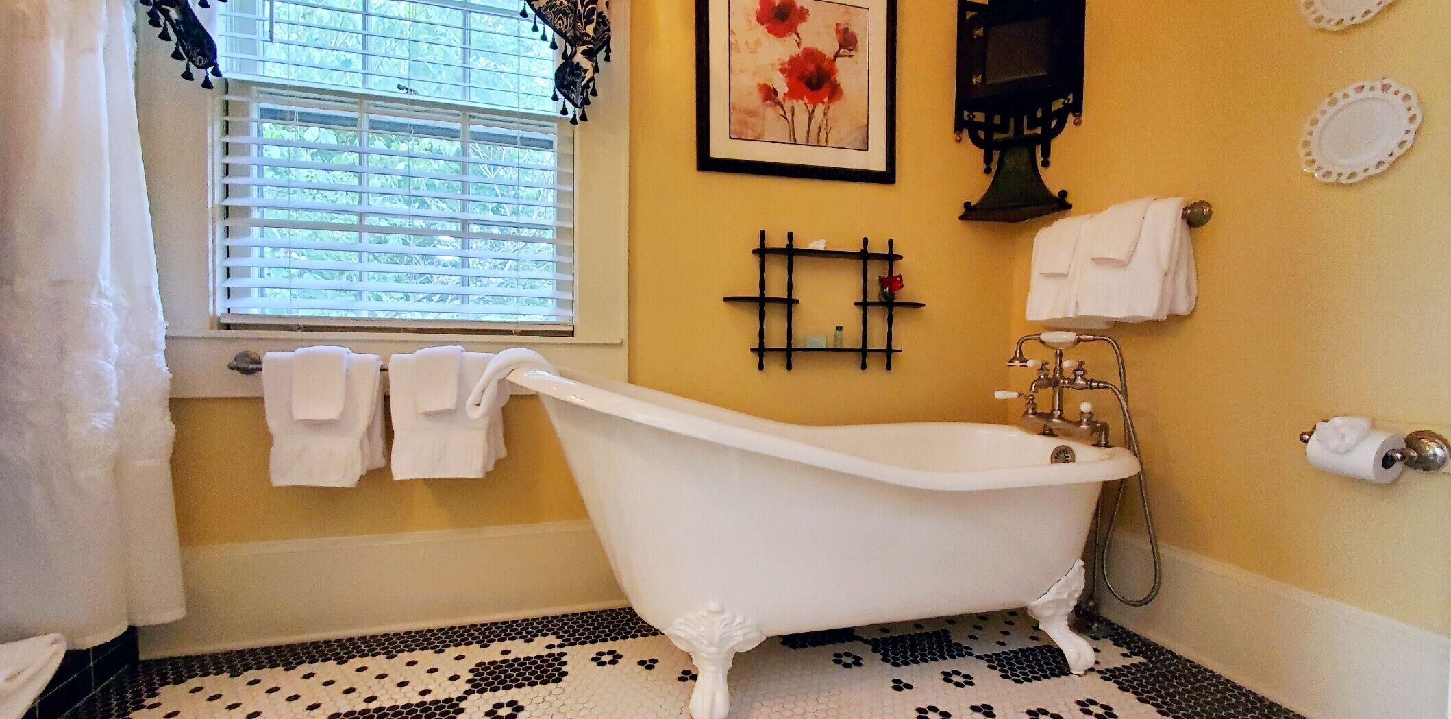 A bathroom with a clawfoot bathtub, a window with blinds, and a tiled floor.