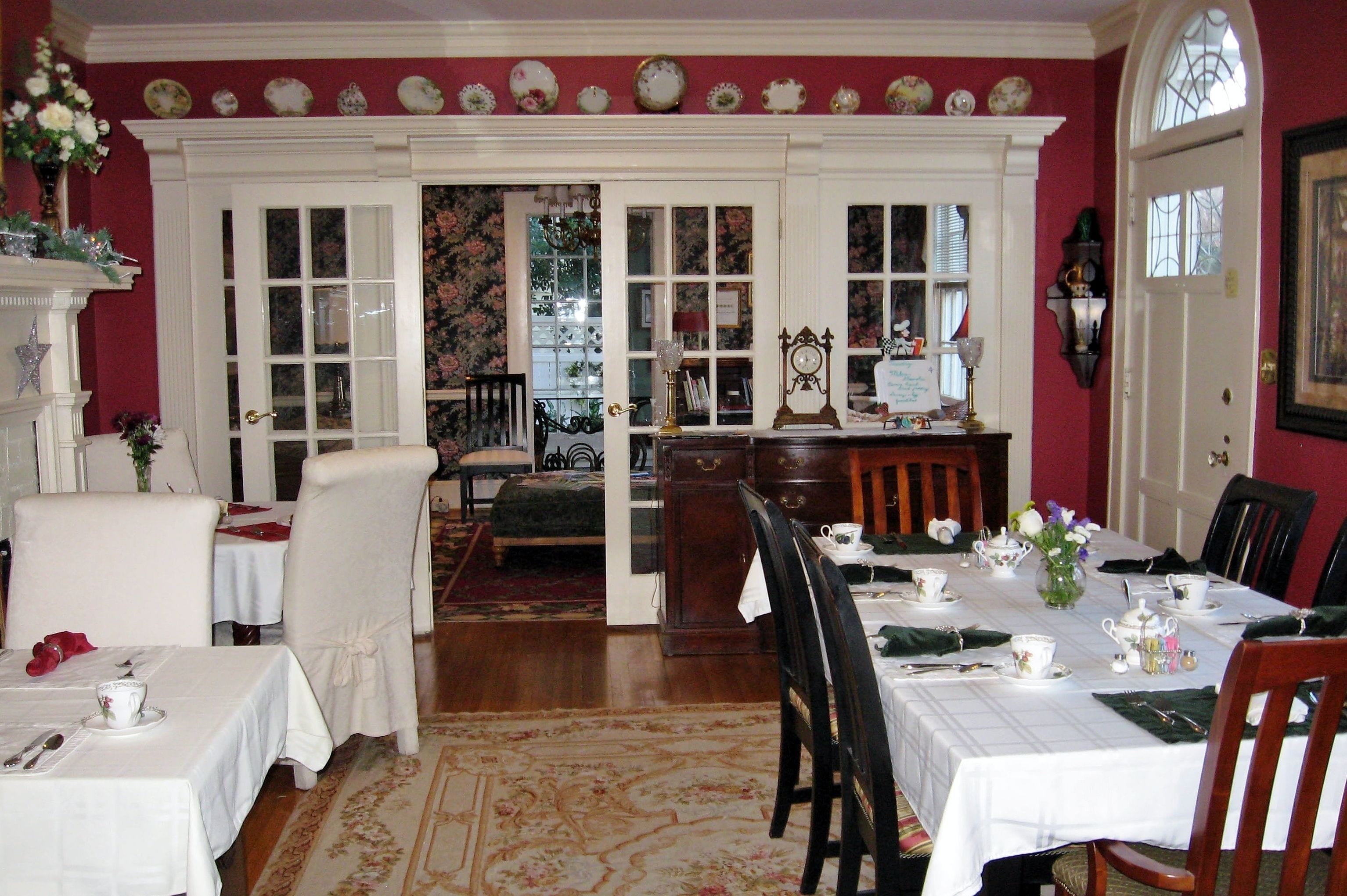 Une salle à manger avec une table dressée pour quatre personnes, une cheminée et une vue sur l’extérieur, visible à travers une porte.