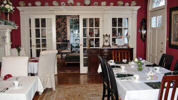 Une salle à manger avec une table dressée pour quatre personnes, une cheminée et une vue sur l’extérieur, visible à travers une porte.
