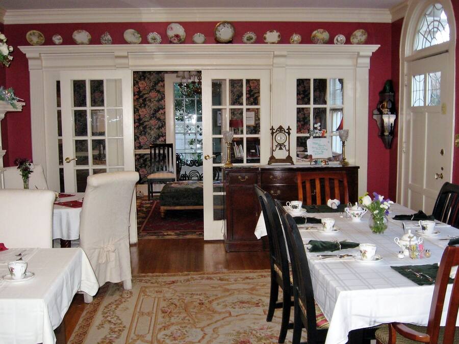 Une salle à manger avec une table dressée pour quatre personnes, une cheminée et une vue sur l’extérieur, visible à travers une porte.