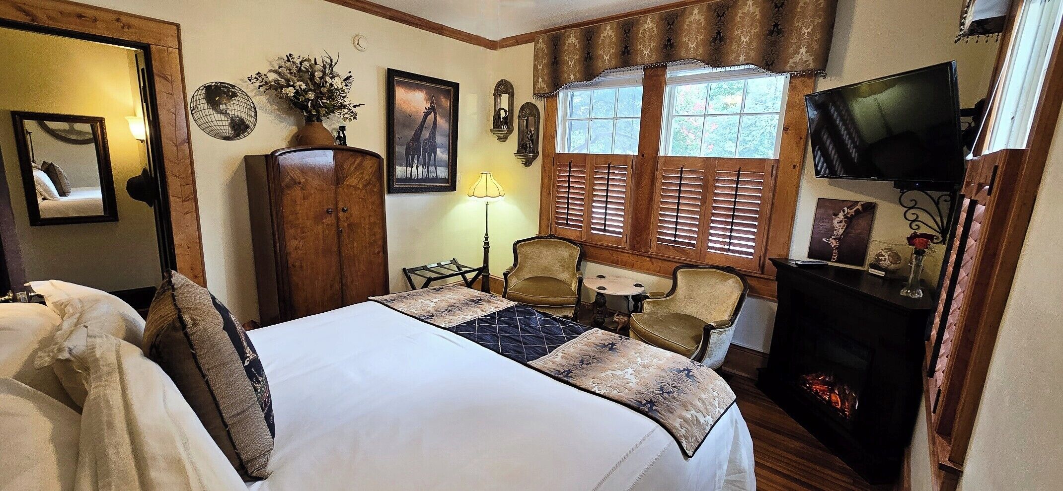 A hotel room with a bed, two chairs, a small table, a TV, and a fireplace.