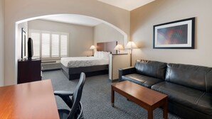 Habitación de hotel con cama, sofá de cuero, escritorio y silla. Se ve una ventana con persianas y un cuadro en la pared.