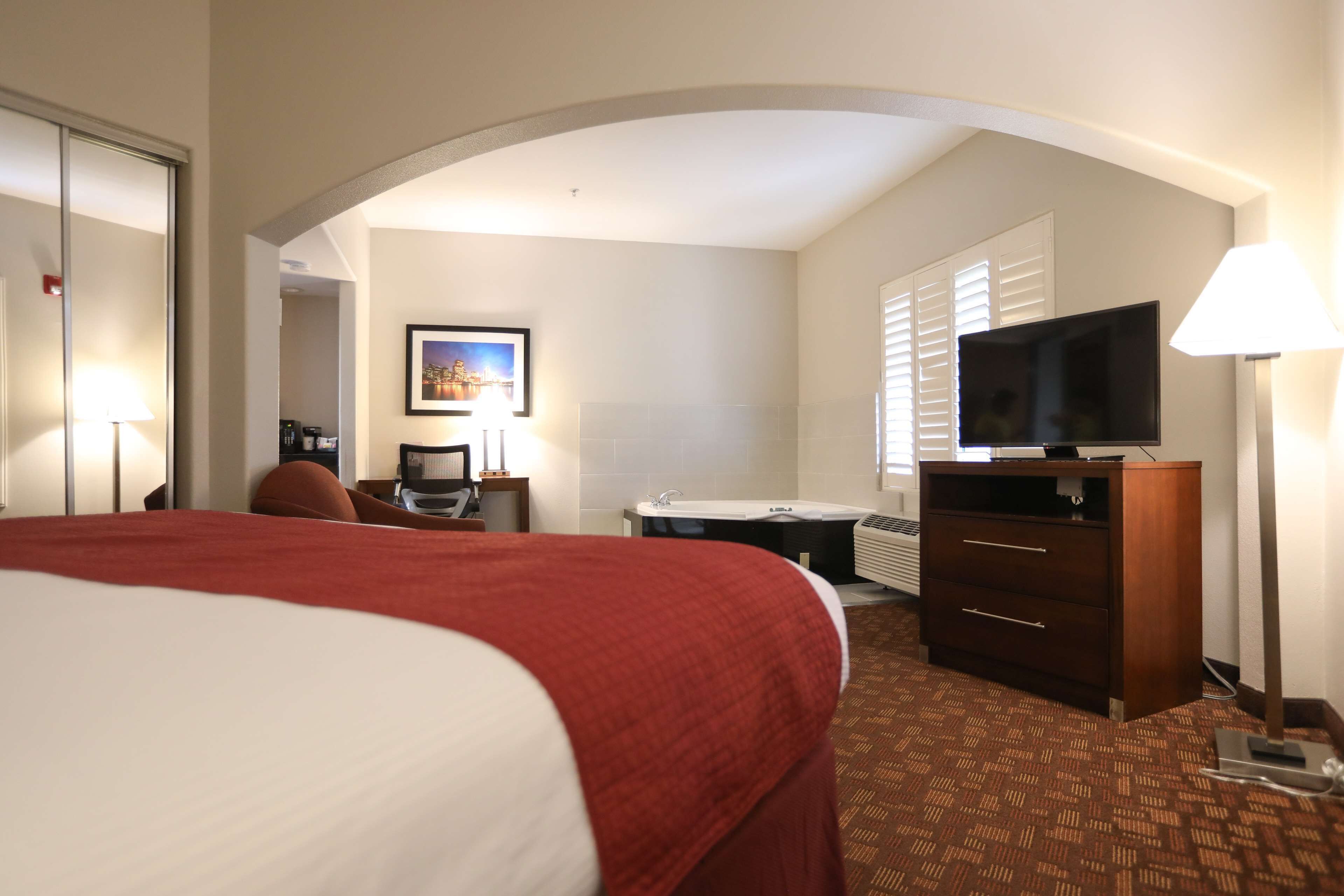Een hotelkamer met een groot bed, een bureau met stoel, een televisie, een dressoir en een badkamer met douche en toilet.