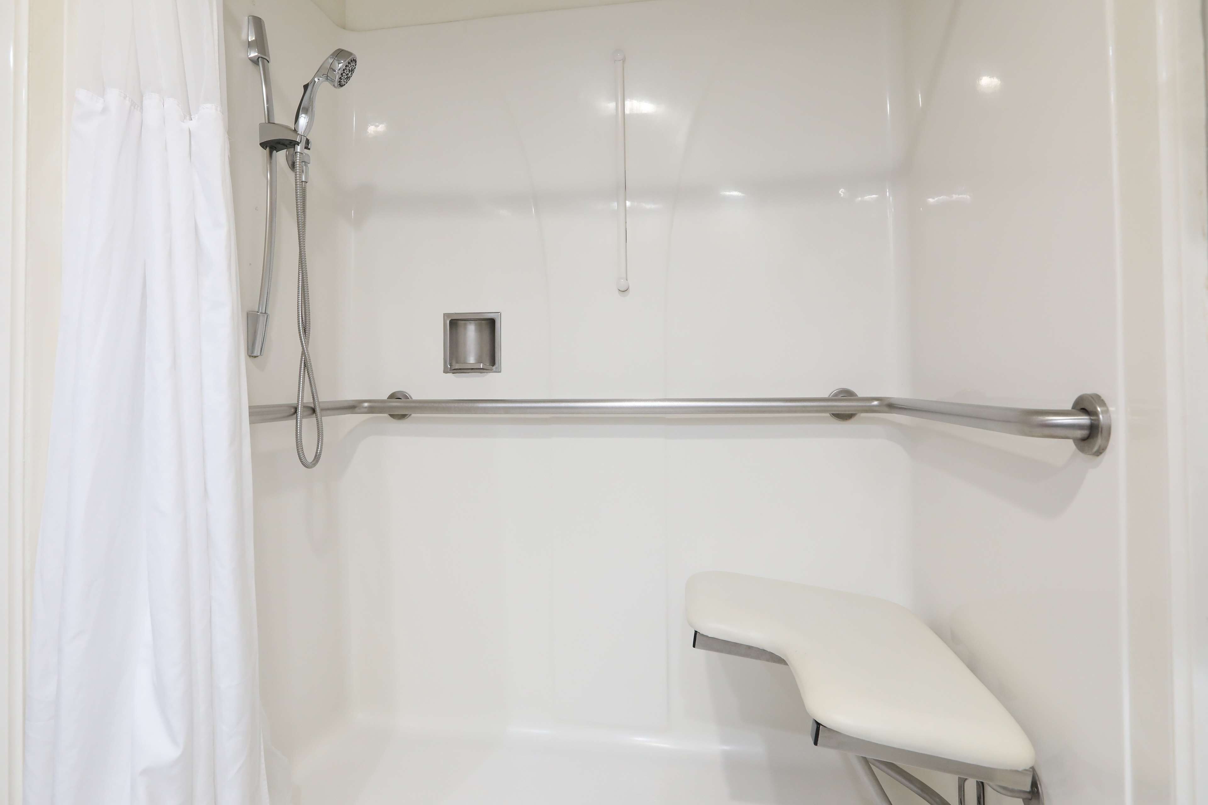 Un área de ducha blanca y cerrada con ducha de mano y barra de apoyo.