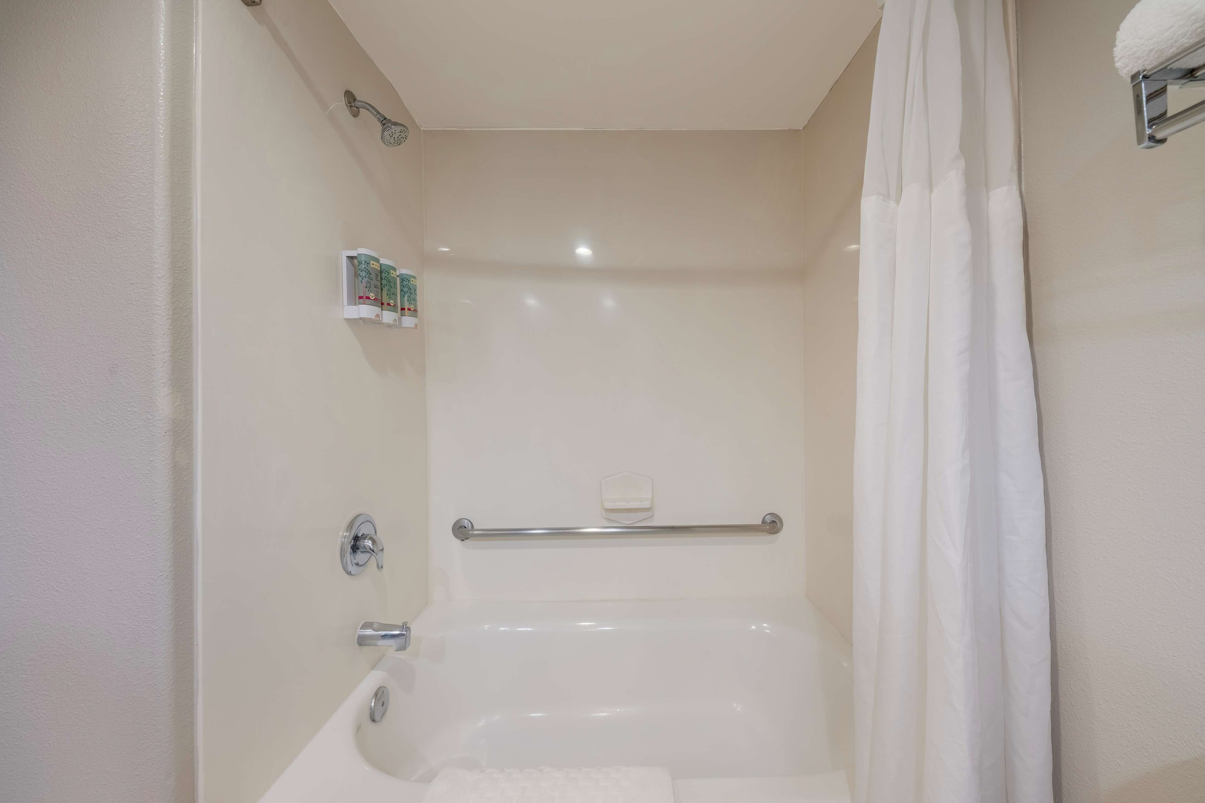A bathroom with a bathtub, a shower curtain, a towel rack, and a soap dispenser.
