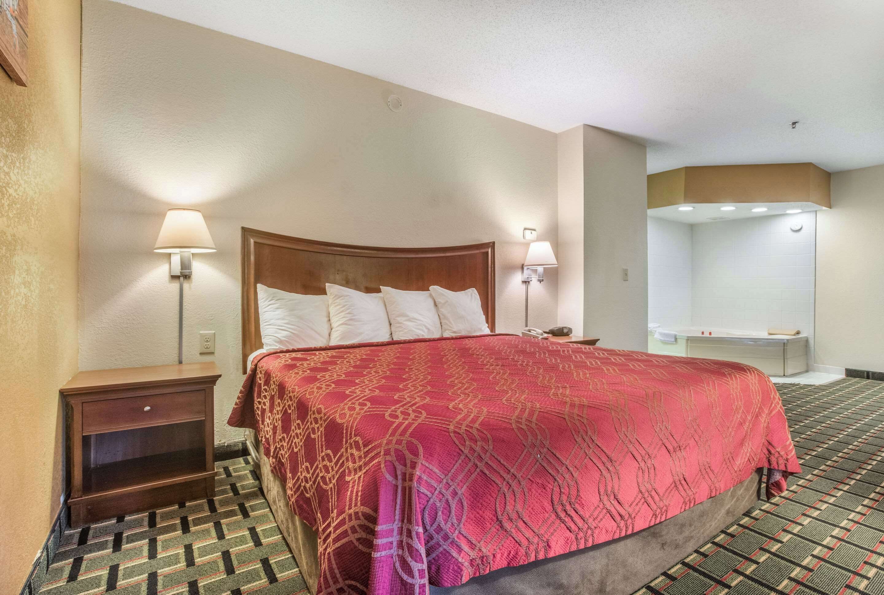 Ein Hotelzimmer mit einem großen Bett, zwei Nachttischlampen, einem Nachttisch und einem Badezimmer mit Badewanne.