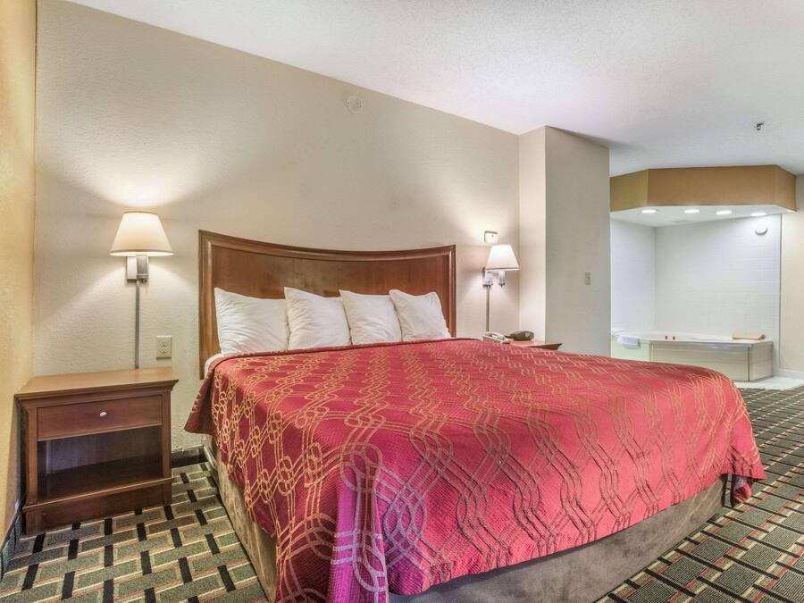 Ein Hotelzimmer mit einem großen Bett, zwei Nachttischlampen, einem Nachttisch und einem Badezimmer mit Badewanne.