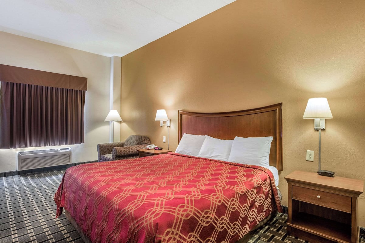 A hotel room with a large bed, two bedside lamps, a chair, and a nightstand.