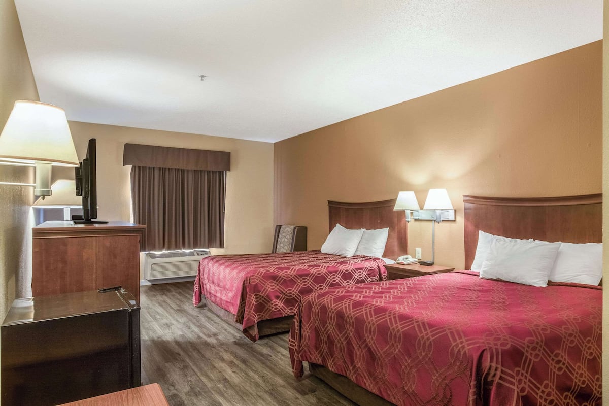 A hotel room with two beds, a desk, a television, and a window with curtains.
