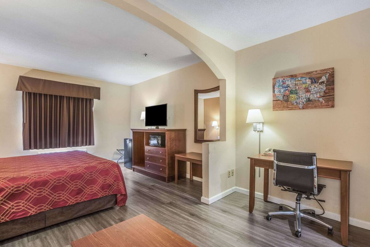 A hotel room with a bed, a desk, a chair, a television, a dresser, and a map artwork on the wall.