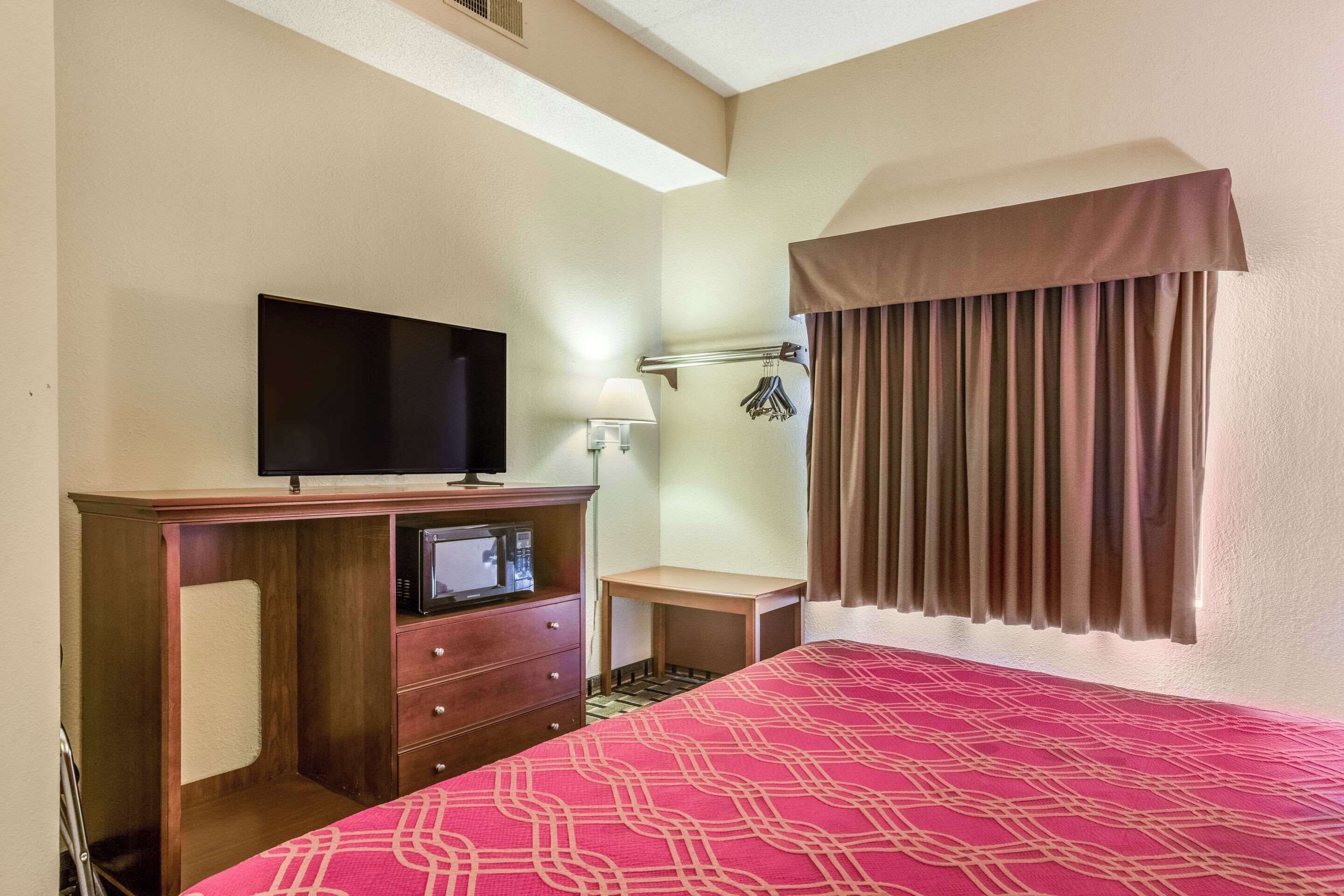 A hotel room with a bed, a TV, a desk with a lamp, and a window with curtains.