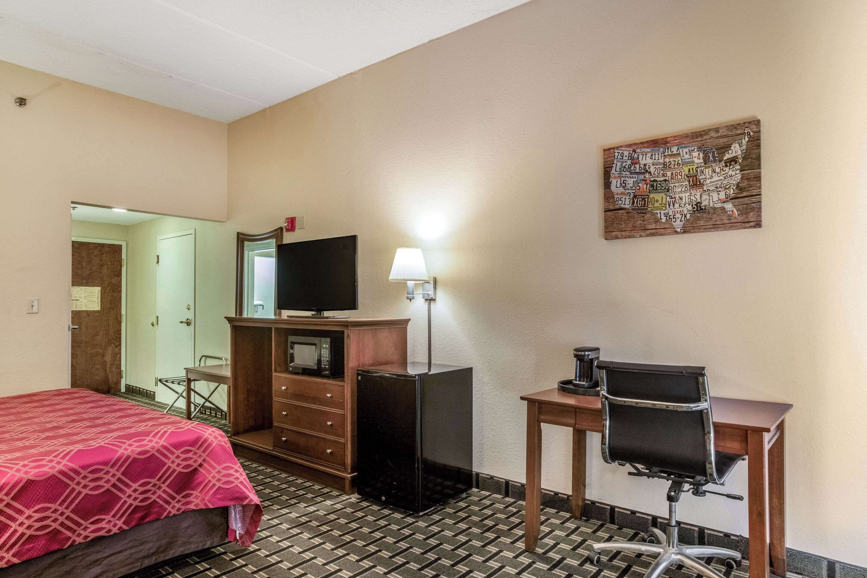 A hotel room with a bed, a desk, a chair, a television, a dresser, and a wall art piece.