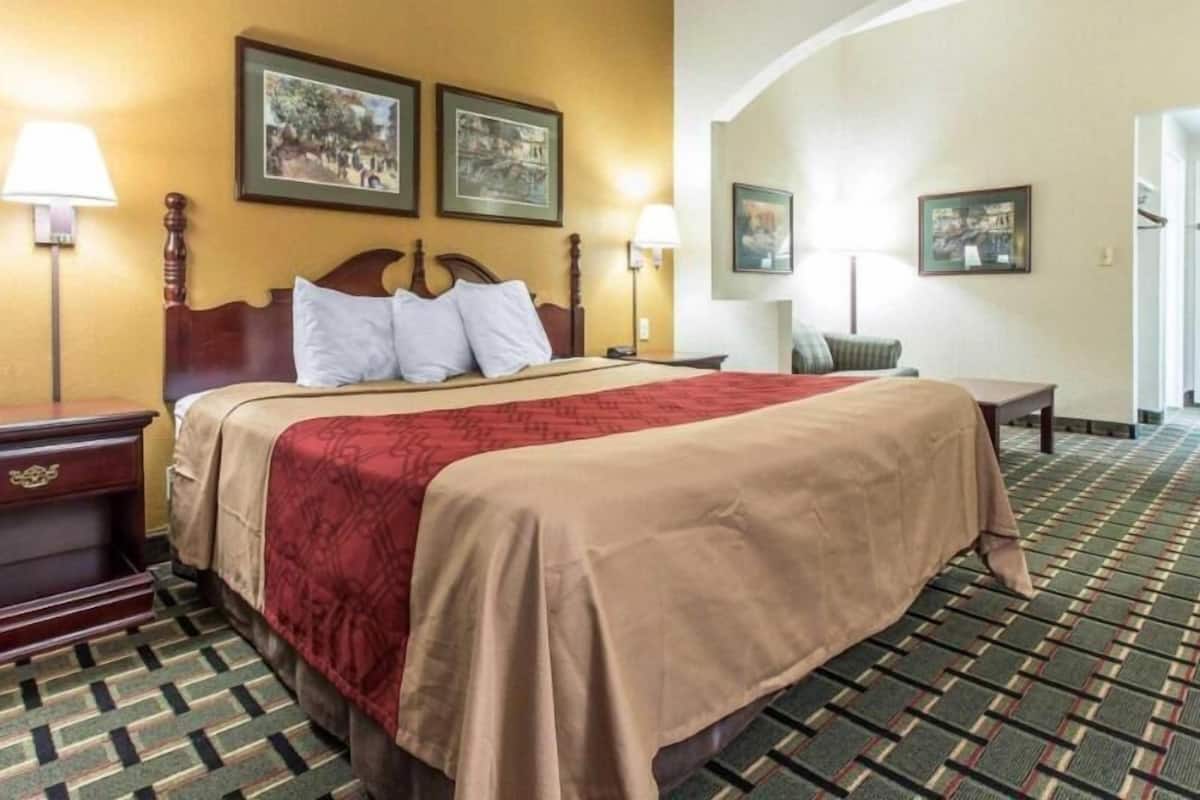 A hotel room with a bed, two wall-mounted lamps, a wooden nightstand, a small table, and two framed pictures on the wall.