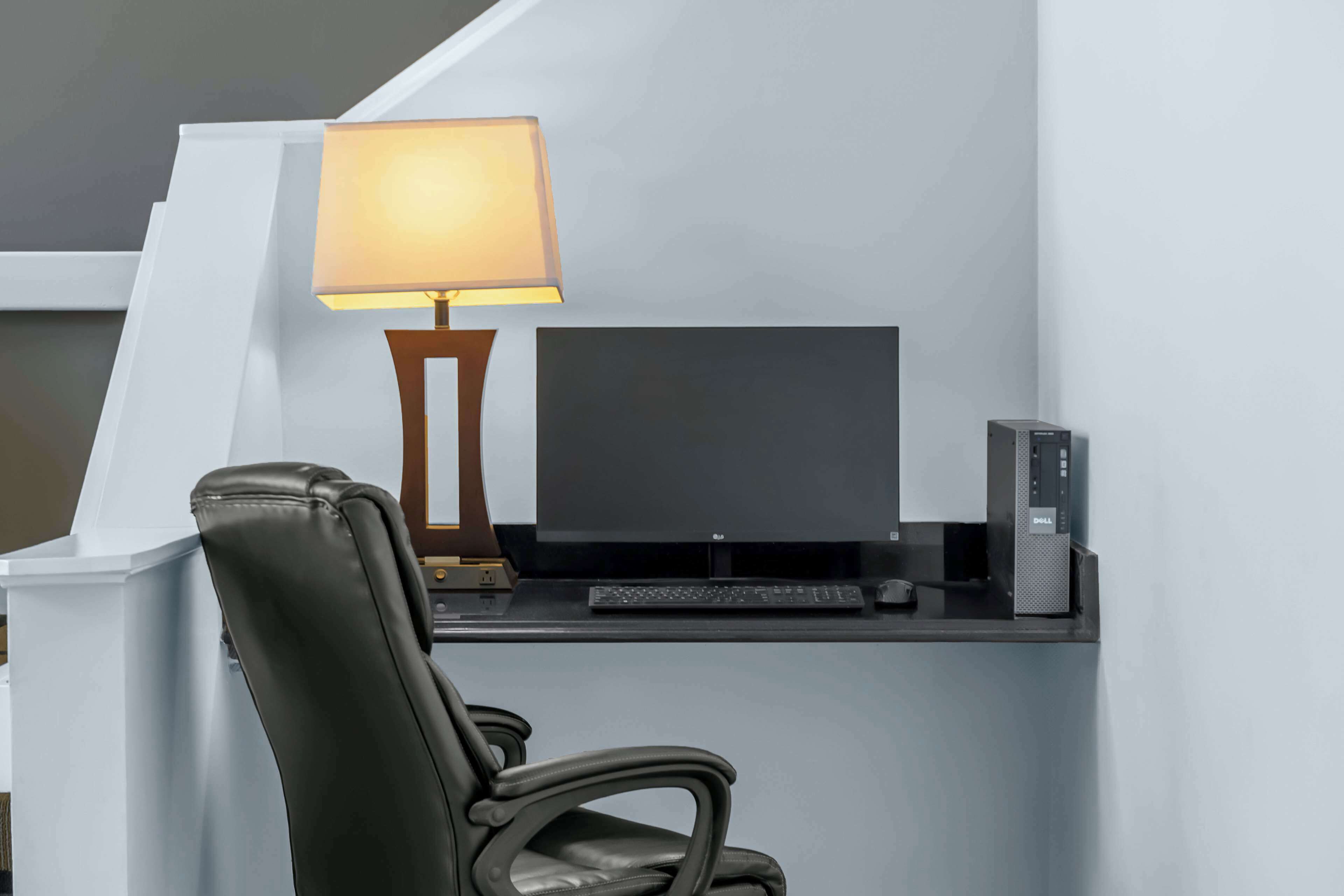 A modern office desk with a computer monitor, keyboard, and a lamp.