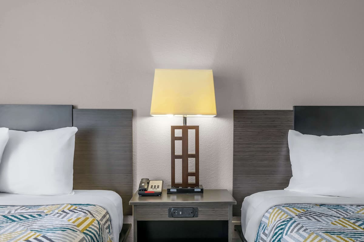 A hotel room with two beds, a nightstand with a lamp, a phone, and a control panel.