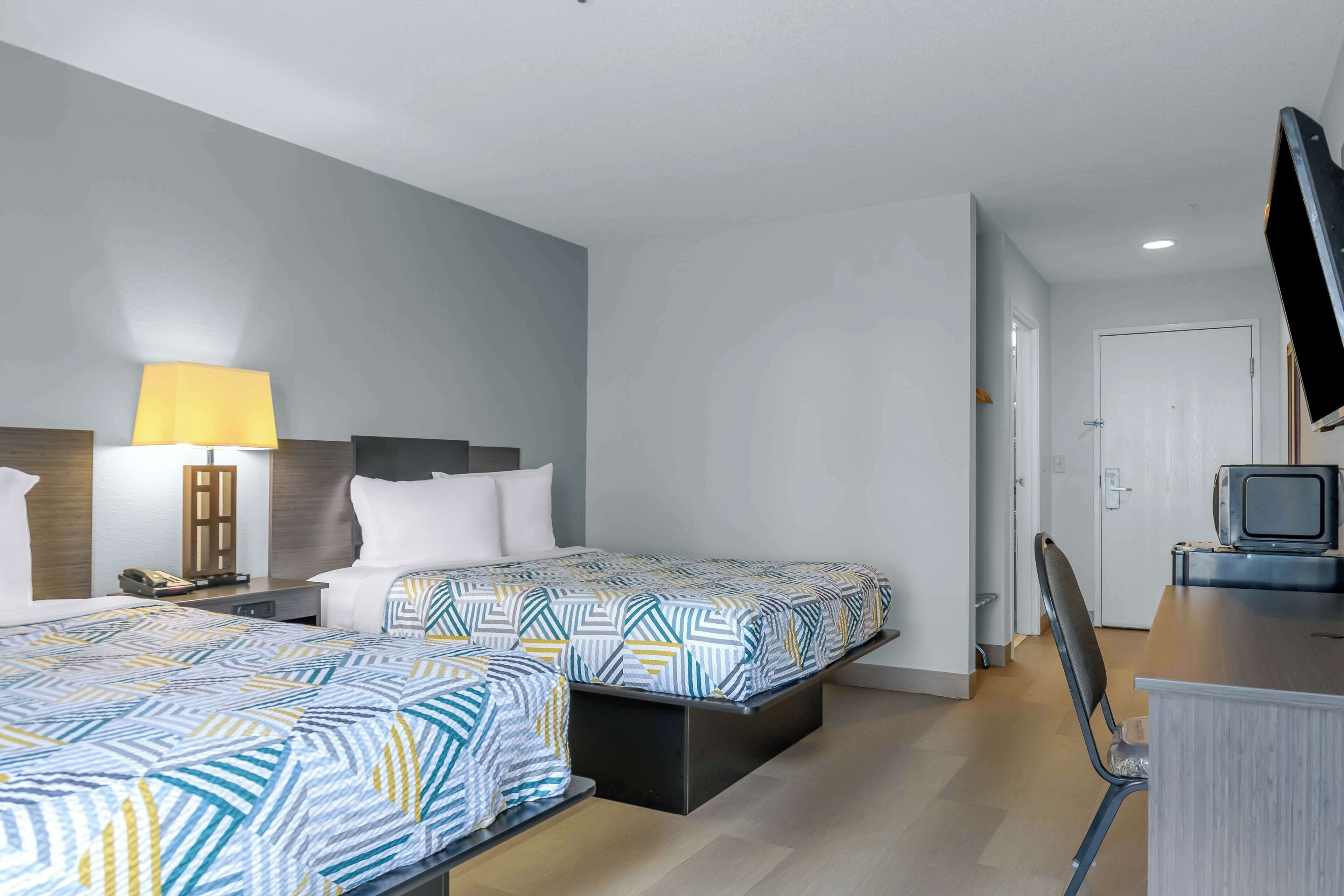 Una habitación de hotel con dos camas, un escritorio con televisor y una lámpara.