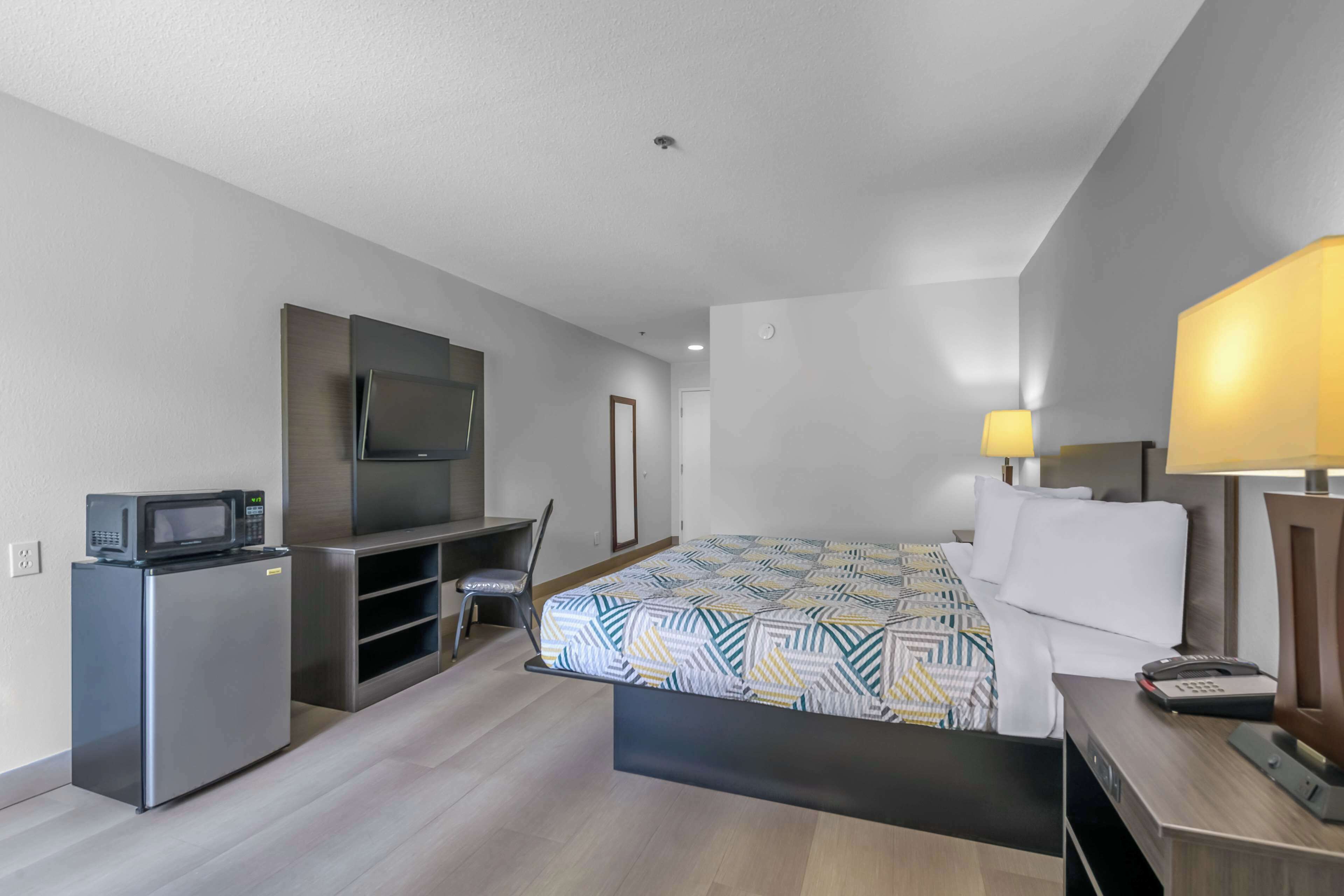 A modern hotel room with a bed, desk, and built-in TV.