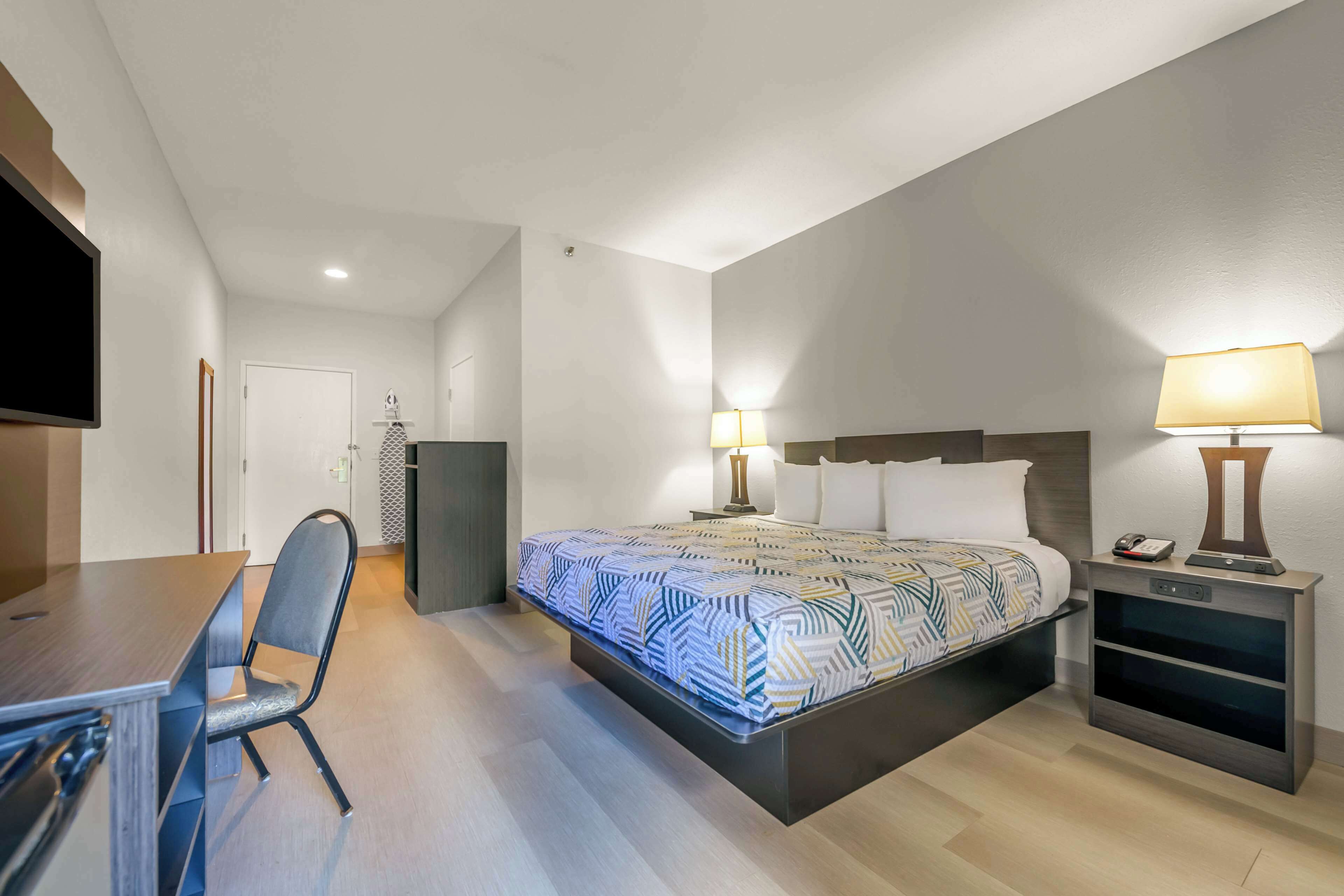 A modern hotel room with a bed, bedside table, lamp, and a TV.