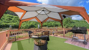 A covered outdoor seating area with a grill and artificial grass.