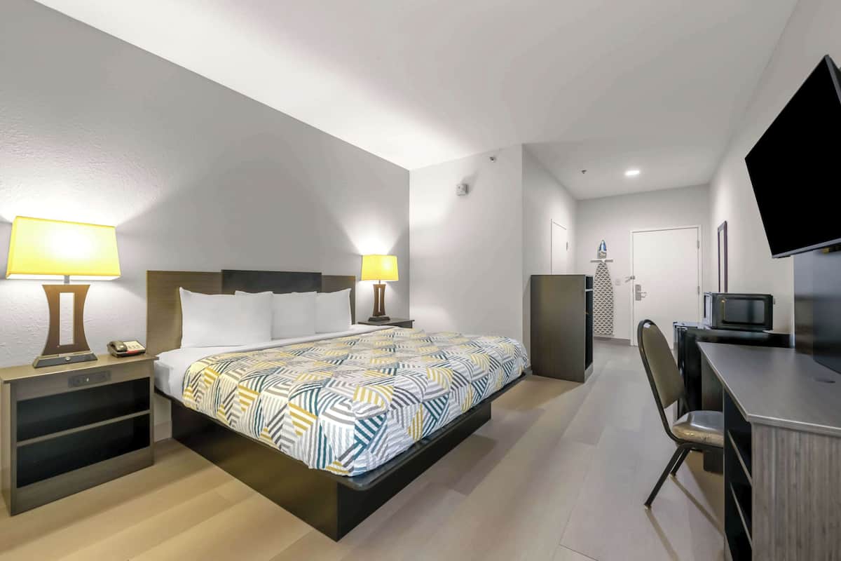A hotel room with a bed, bedside lamps, a desk with a chair, a television, and a door leading to a bathroom.