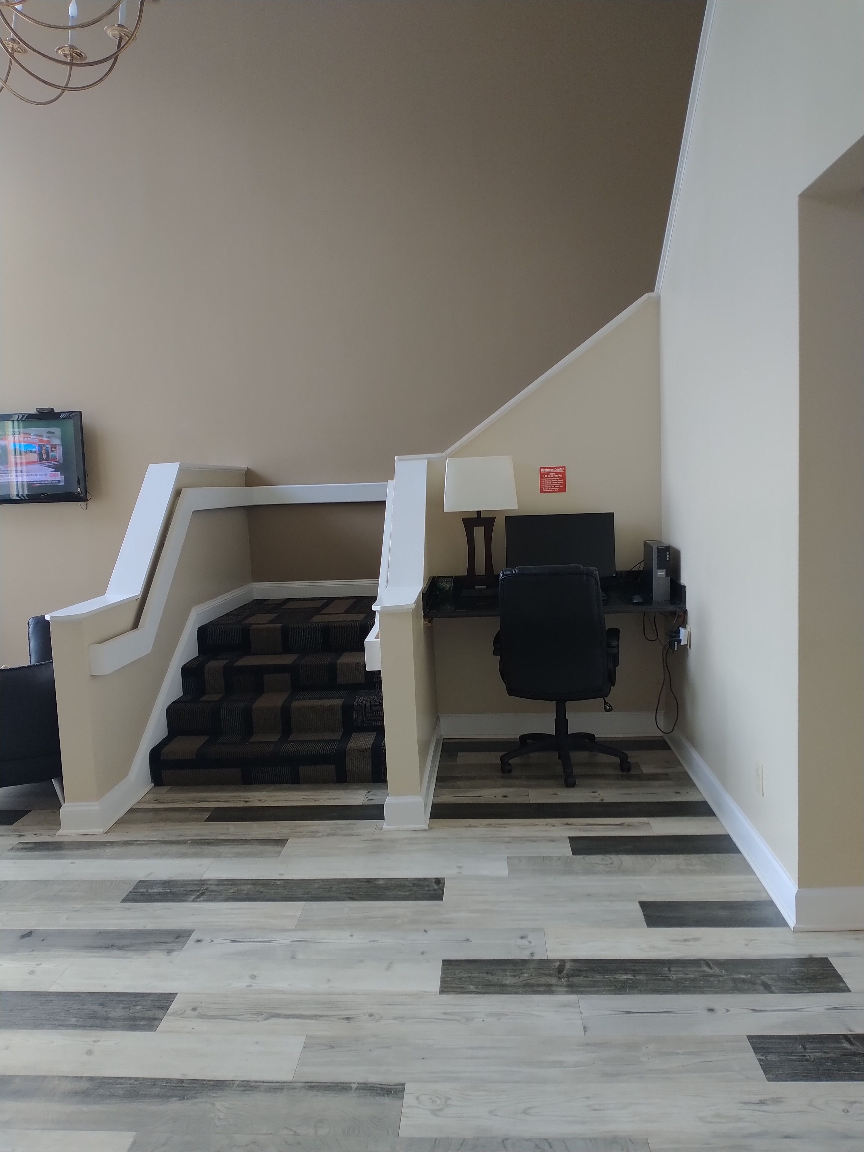 A hotel room with a staircase, a desk with a computer, a chair, and a television on the wall.