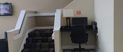 A hotel room with a staircase, a desk with a computer, a chair, and a television on the wall.
