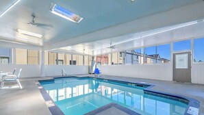 An indoor swimming pool with clear blue water, surrounded by white walls and large windows.