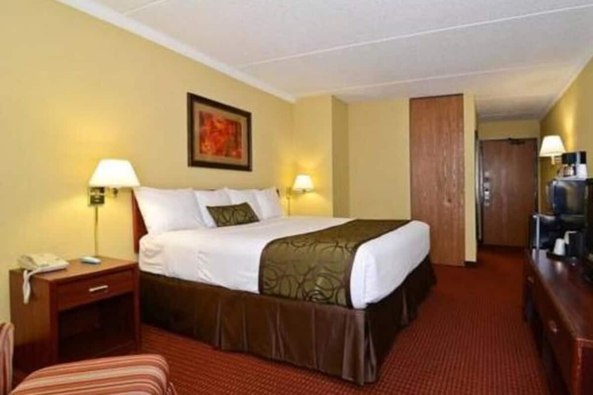 A hotel room with a bed, bedside lamps, a desk, a chair, and a television.