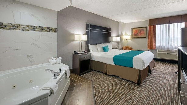 A hotel room with a large bed, a separate bathroom with a bathtub, a desk with a computer, and a window with curtains.